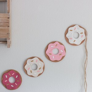 K&ouml;nnte beinhalten: Eine Girlande aus Filzdonuts mit rosa und wei&szlig;em Zuckerguss und goldenen Streuseln. Die Donuts sind mit einer Schnur aneinandergereiht.