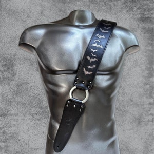 May include: Black leather guitar strap with silver bats embossed on the strap. The strap has a silver metal adjustable buckle.