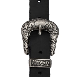 May include: A black leather belt with a silver ornate buckle. The buckle has a floral design and a rectangular piece with a floral design.