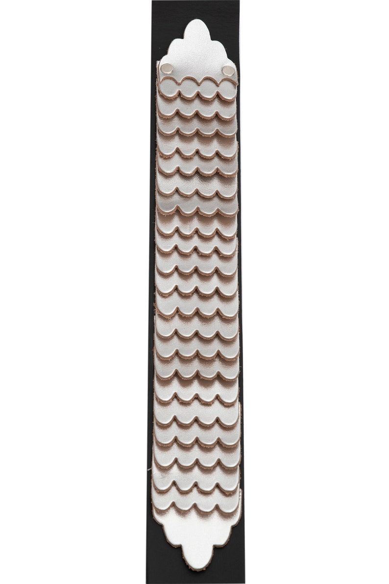 May include: A silver leather bracelet with a scalloped design. The bracelet is attached to a black leather strap.