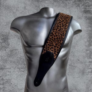 Puede incluir: Una correa de guitarra de cuero negro con un diseño de estampado de leopardo marrón.