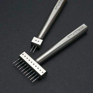 May include: Two leather crafting tools, one with a single punch and the other with multiple punches. The tools are made of metal and have a silver finish. The tool with multiple punches has the text "KS Blade Punch" engraved on the handle.