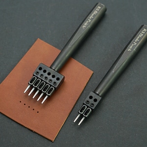 May include: Two black leather punch tools with metal blades. The larger tool has six blades and the smaller tool has three blades. Both tools have "KS Blade Punch" engraved on the handles.