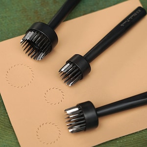 May include: Three black leather hole punch tools with circular blades. The tools are on a light brown surface with three circles of stitching around the holes.