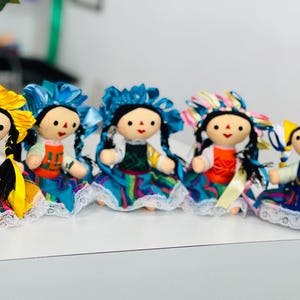 May include: Six colourful handmade rag dolls with embroidered details and braided hair. The dolls are wearing colourful skirts and have different coloured hair and clothing.