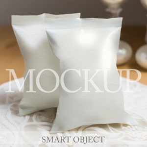 May include: Two white, blank, stand-up pouches on a white lace surface. The pouches are made of a thin, flexible material and have a matte finish. The pouches are perfect for packaging small items, such as snacks, candy, or jewelry.  The text "MOCKUP" is superimposed on the image.