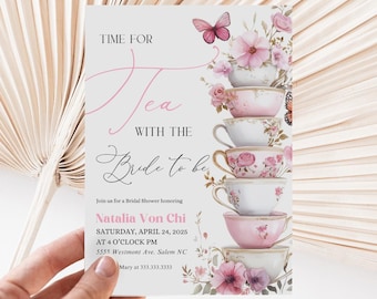 May include: A bridal shower invitation with a pink and white teacup theme. The invitation features a stack of teacups with pink flowers and butterflies. The text reads "Time for Tea with the Bride to be" and includes the bride's name, date, time, and location.