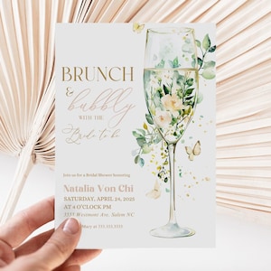 May include: A white invitation card with a gold and pink design. The card features a glass of champagne with flowers and greenery inside. The text on the card reads "BRUNCH & bubbly with the Bride to be" and includes the details for a bridal shower honouring Natalia Von Chi.