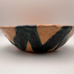 May include: A handmade ceramic bowl with a tan exterior and dark green geometric patterns. The bowl has a wide, shallow shape and a slightly irregular rim, showcasing its artisanal quality. The interior is a light tan colour.