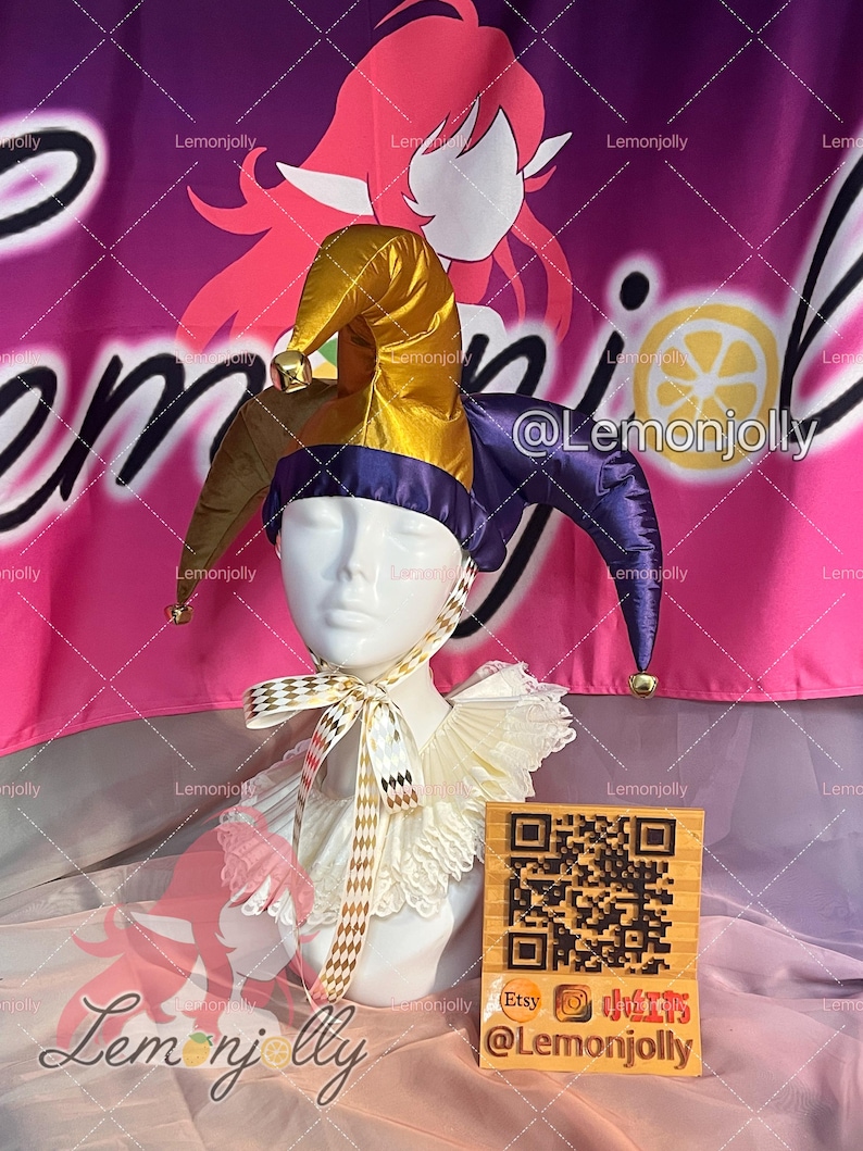 May include: A jester's hat with gold, brown, and purple panels, adorned with small bells. The hat is displayed on a mannequin head, paired with a white ruffled collar and a checkered ribbon. A wooden block with a QR code and social media handles is in the foreground.