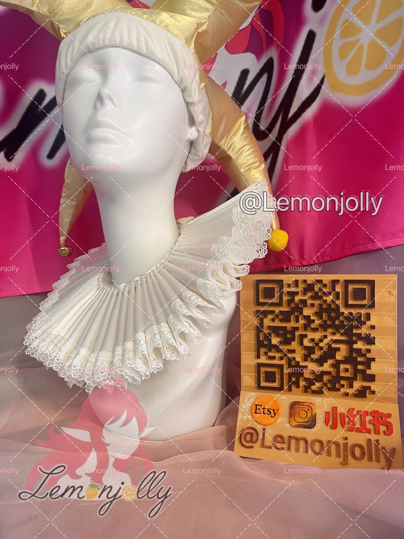 May include: A white pleated ruff collar with delicate lace trim worn by a white mannequin head. The mannequin wears a gold jester hat with small yellow bells. A wooden sign with a QR code and the text Etsy, Instagram, and Lemonjolly is present.
