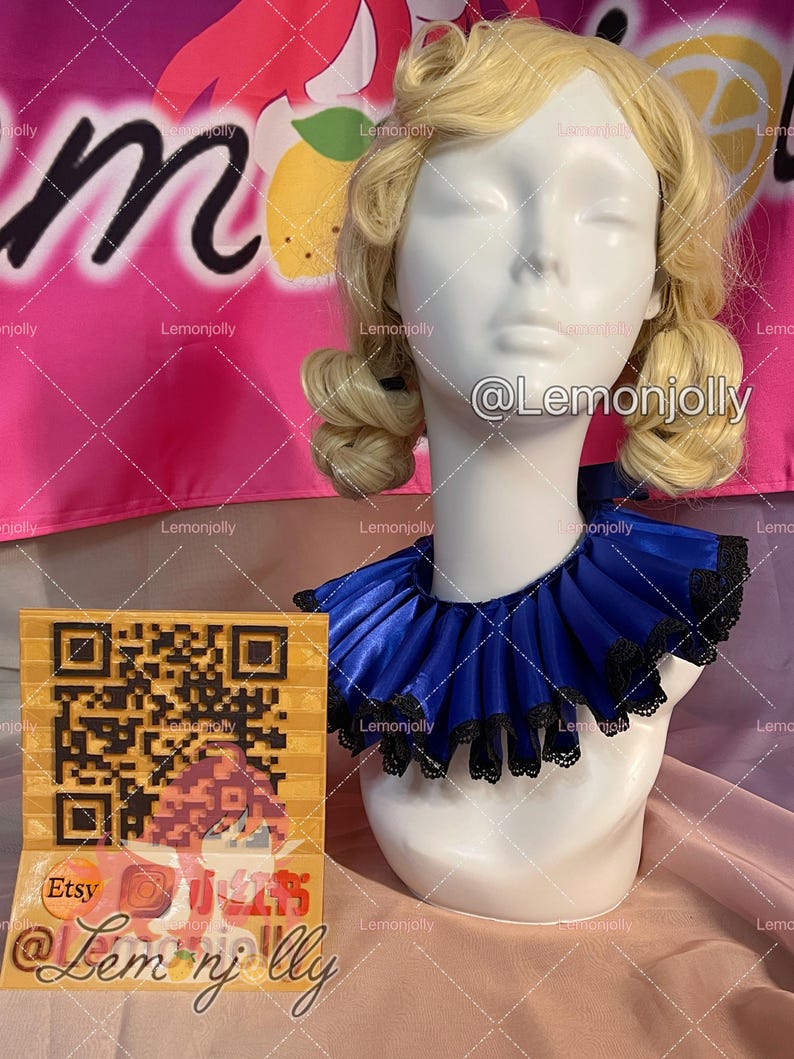 May include: A white mannequin head with blonde hair wearing a royal blue satin ruff collar featuring a black lace trim along the edges. The collar is pleated and sits around the neck of the mannequin. A square card with a QR code is visible.