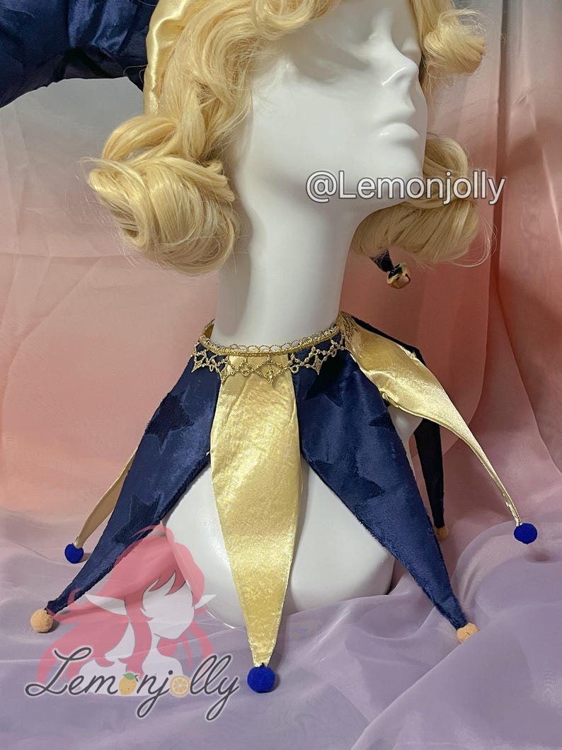 May include: A jester collar featuring alternating navy blue velvet and gold satin points. The navy blue points have a subtle star pattern. The collar is accented with a gold lace trim at the neck and small blue and beige pom-poms at each tip. Text reads @Lemonjolly.