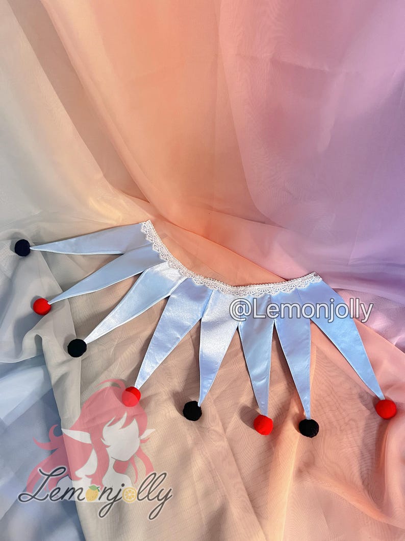 May include: A light blue jester collar featuring a white lace trim along the neckline and alternating black and red pom-poms at the tips of each pointed segment. The text @Lemonjolly is visible on the right side of the collar.