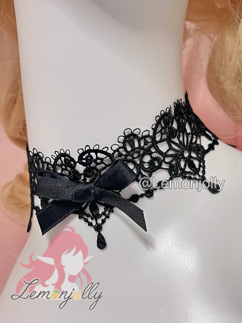 May include: A black lace choker necklace featuring an intricate floral pattern with scalloped edges and a small black satin ribbon bow attached to the front. The design includes delicate dangling lace accents and the text @Lemonjolly.