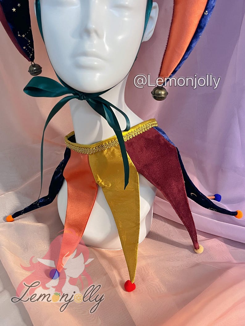 May include: A jester hat and collar set featuring a multi-colored design with velvet and satin fabrics. The hat has dark blue star-patterned points with bells, while the collar features gold, orange, and burgundy points with colorful pom-poms. Text reads @Lemonjolly.