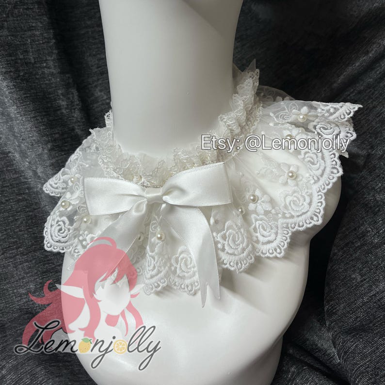 May include: A white lace collar featuring a scalloped edge with floral embroidery, small faux pearls, and a central satin ribbon bow. The collar is displayed on a mannequin neck and includes the text Etsy: @Lemonjolly and a logo.