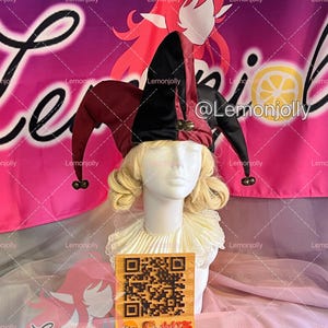 May include: A jester hat with black and burgundy panels and bells, displayed on a mannequin head with a blonde wig and a white ruffled collar. The background features a pink banner with the text "Lemonjolly".