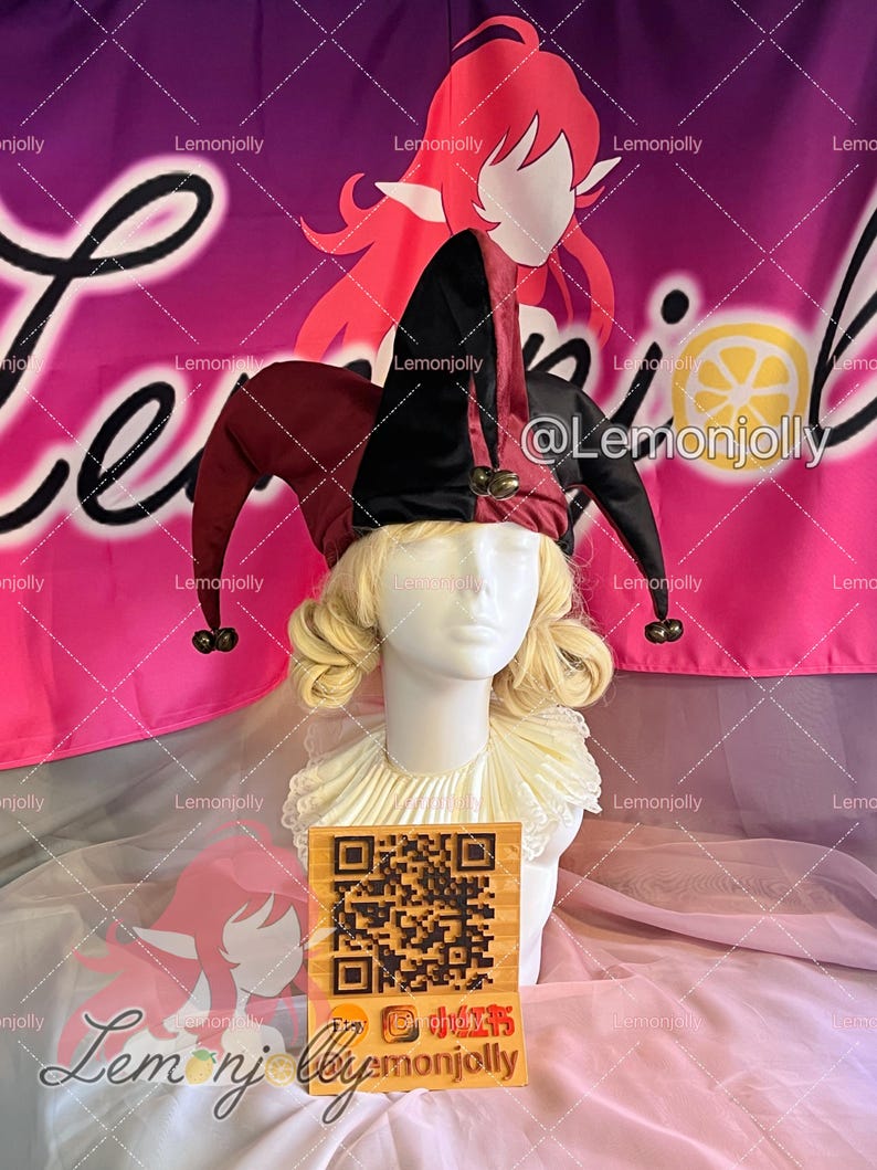 May include: A jester hat with black and burgundy panels and bells, displayed on a mannequin head with a blonde wig and a white ruffled collar. The background features a pink banner with the text "Lemonjolly".