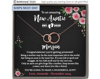 May include: A rose gold-toned necklace with two interlocking circular pendants presented in a gift box. The card features pink floral illustrations and text reading: To an amazing New Auntie EST. 2025, Morgan, and a message about being a wonderful aunt.