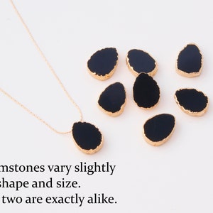 K&ouml;nnte beinhalten: Eine goldene Halskette mit einem schwarzen tropfenf&ouml;rmigen Edelsteinanh&auml;nger und sechs weiteren losen schwarzen Edelsteinen mit goldfarbenen R&auml;ndern. Der Text lautet: Gemstones vary slightly in shape and size. No two are exactly alike.