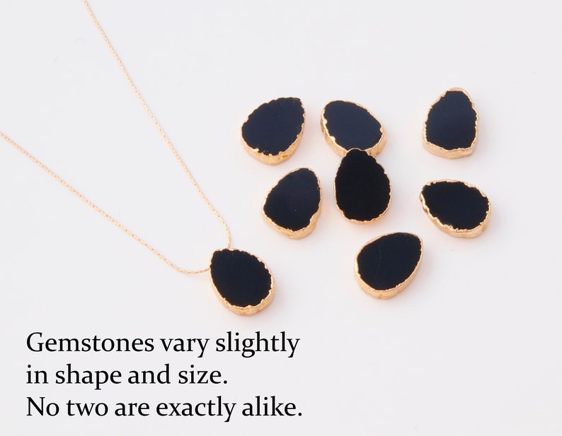K&ouml;nnte beinhalten: Eine goldene Halskette mit einem schwarzen tropfenf&ouml;rmigen Edelsteinanh&auml;nger und sechs weiteren losen schwarzen Edelsteinen mit goldfarbenen R&auml;ndern. Der Text lautet: Gemstones vary slightly in shape and size. No two are exactly alike.