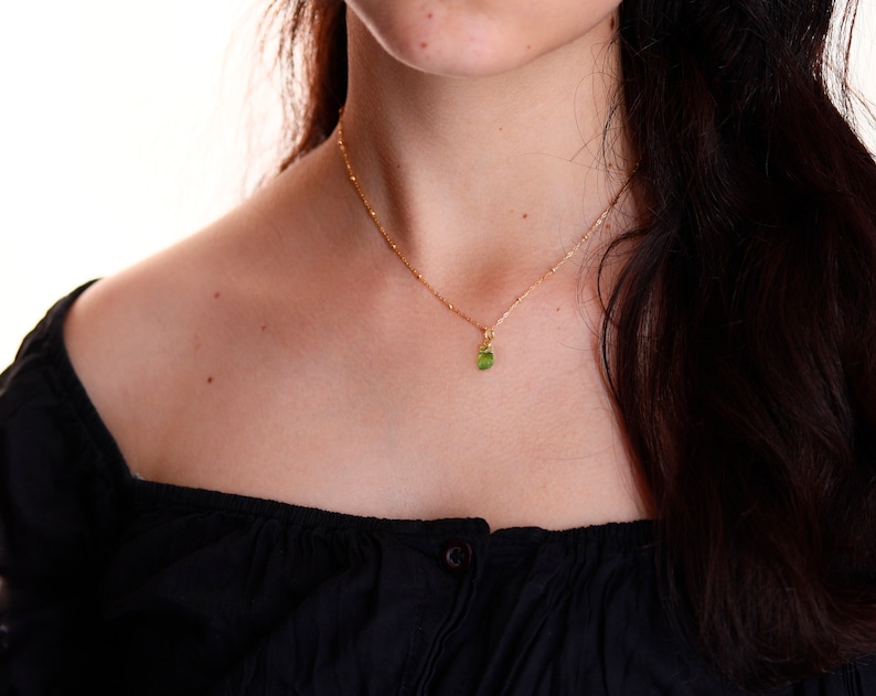 May include: A gold chain necklace with a small green gemstone pendant.