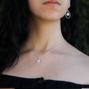 May include: A silver necklace with a pearl pendant and a circle design. The necklace is worn by a person with long dark hair.