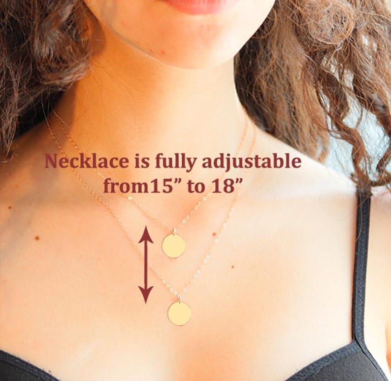 May include: A gold-toned necklace featuring two delicate chains, each with a small, circular pendant. The text on the image states: Necklace is fully adjustable from 15" to 18". A vertical arrow indicates the adjustable length of the chain.