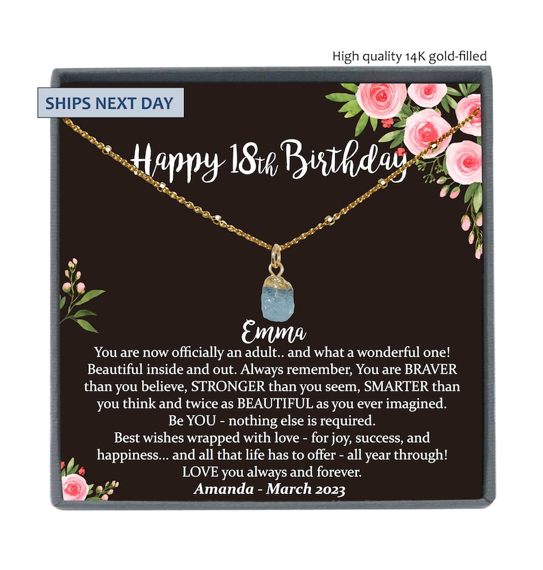 May include: A gold necklace with a light blue gemstone pendant in a black box with a floral design. The box has the text "Happy 18th Birthday" and "Emma" on it.