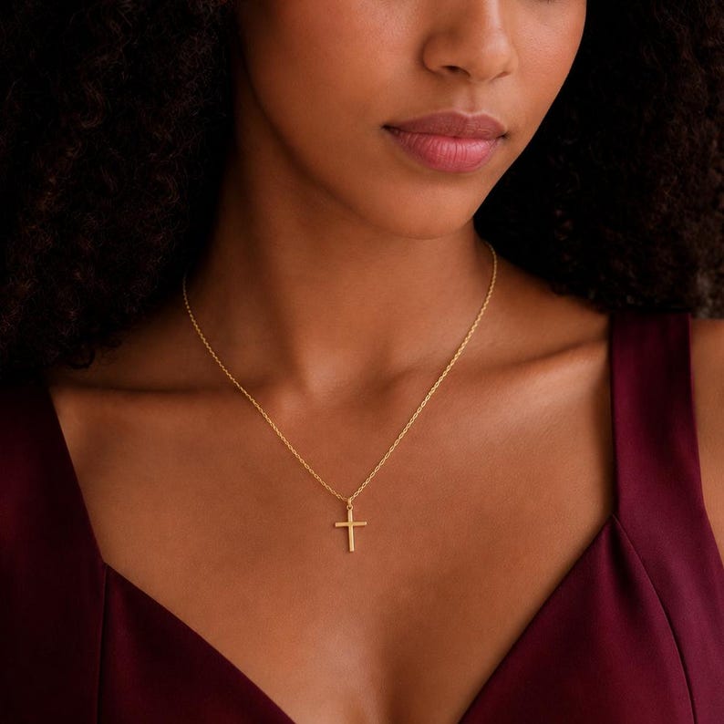 May include: A gold-toned metal necklace featuring a simple, plain cross pendant suspended from a delicate, thin chain. The cross has a smooth, polished finish and is centered on the chain, which rests against the collarbone area of the neck.