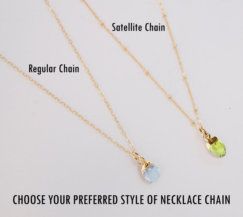 May include: Two gold necklaces with different chain styles: a regular chain and a satellite chain. Both necklaces have a small gemstone pendant attached.