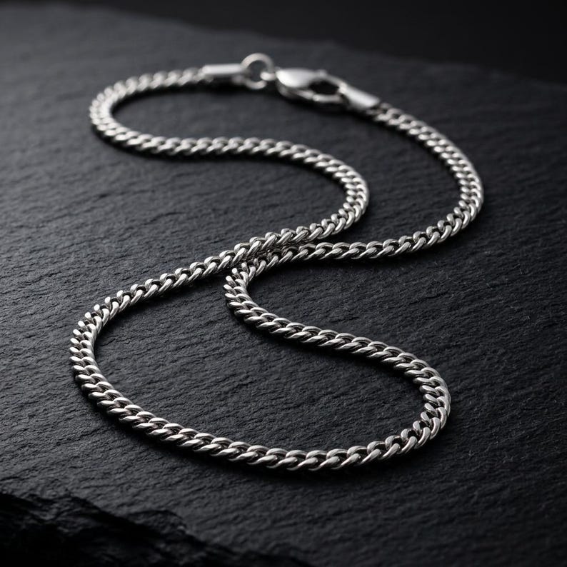 May include: A silver-toned metal chain necklace featuring a classic curb link design. The chain is constructed with uniform, interlocking oval links and is secured with a functional lobster claw clasp mechanism at the end of the metal strand.