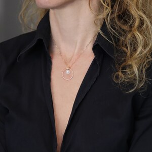 May include: A delicate gold necklace with a small pearl pendant hanging from a circle charm.