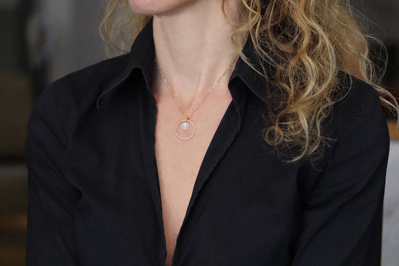 May include: A delicate gold necklace with a small pearl pendant hanging from a circle charm.