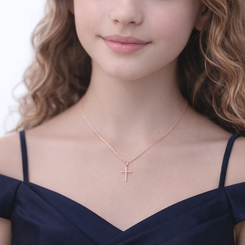 Puede incluir: Un collar con colgante de cruz de oro rosa. La cruz tiene un dise&ntilde;o sencillo, suspendido de una delicada cadena. El collar se lleva con un vestido azul oscuro.