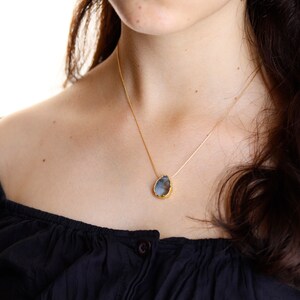 May include: A gold chain necklace with a teardrop-shaped pendant featuring a grey stone.