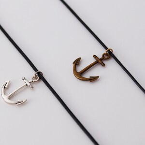 May include: Two black cords with silver and bronze anchor charms hanging from them.