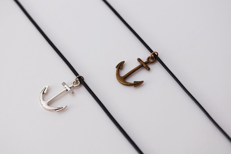May include: Two black cords with silver and bronze anchor charms hanging from them.