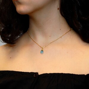 May include: A delicate gold chain necklace with a small, light blue gemstone pendant.