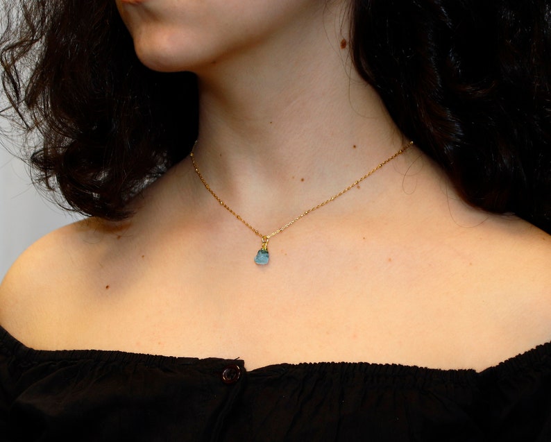 May include: A delicate gold chain necklace with a small, light blue gemstone pendant.