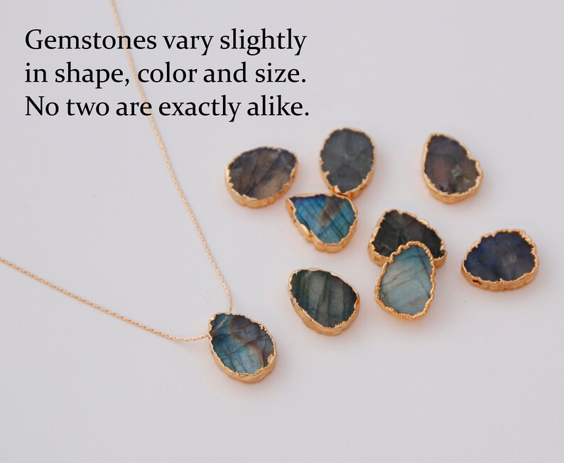 May include: A gold chain necklace with a large, iridescent, teardrop-shaped gemstone pendant. The pendant is surrounded by a thin gold border. The image also shows several other similar gemstones, all with different shapes and colors.