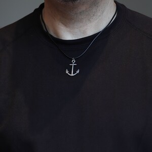 May include: A silver anchor pendant necklace on a black cord.