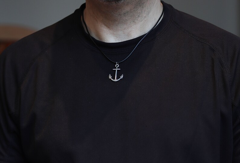 May include: A silver anchor pendant necklace on a black cord.