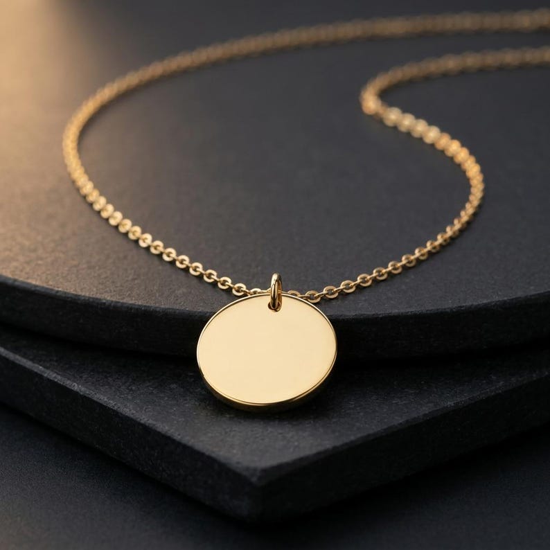 May include: A gold-toned necklace featuring a delicate chain and a smooth, circular pendant. The round charm is polished and reflective, hanging from a small jump ring attached to the chain. The metal has a warm, metallic yellow finish throughout.