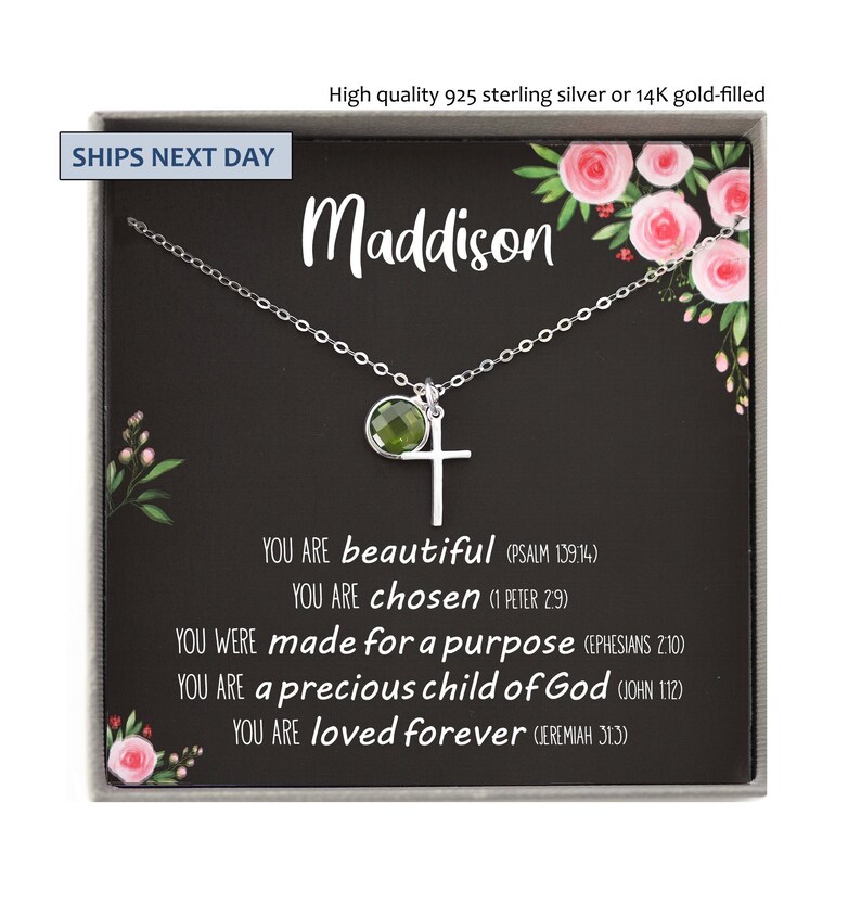 May include: A sterling silver necklace with a cross pendant and a green gemstone. The necklace is presented in a gift box with the name "Maddison" and inspirational text. The box is decorated with floral accents.