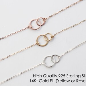 May include: Three delicate chain necklaces, each featuring two interlocking circular rings as a central pendant. The top necklace is rose gold, the middle is yellow gold, and the bottom is silver. Text reads: High Quality 925 Sterling Silver or 14Kt Gold Fill (Yellow or Rose Gold).