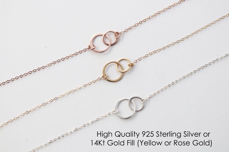 May include: Three delicate chain necklaces, each featuring two interlocking circular rings as a central pendant. The top necklace is rose gold, the middle is yellow gold, and the bottom is silver. Text reads: High Quality 925 Sterling Silver or 14Kt Gold Fill (Yellow or Rose Gold).