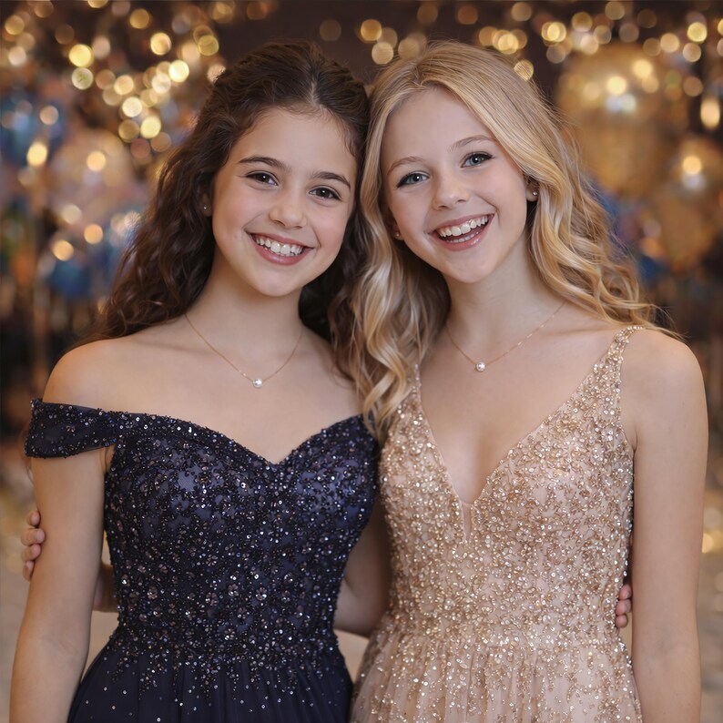 May include: Two young women smiling, wearing formal dresses. One dress is navy blue, off-the-shoulder, and embellished with sequins. The other is a champagne color, sleeveless, and also covered in sequins. Both wear delicate pearl necklaces.