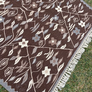 Puede incluir: Una alfombra de color marr&oacute;n y crema con un borde de flecos. La alfombra presenta un dise&ntilde;o floral con hojas y flores.
